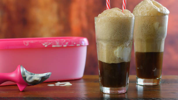 Preparing black cow cola ice cream soda floats against rustic wood background.